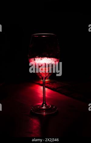 Silhouette di un bicchiere di vino su un tavolo di legno. Luce rossa predominante. Fotografia da bere. Foto Stock