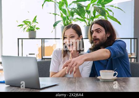 Felice sorprese una giovane coppia che guardava insieme un notebook mentre era seduta in una caffetteria Foto Stock