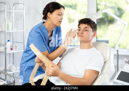Giovane cosmetologa che esamina il volto di un giovane uomo Foto Stock