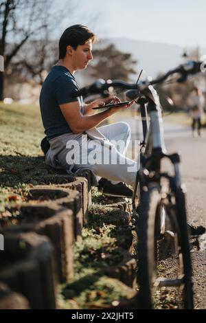 Giovane con una bicicletta che usa uno smartphone in un parco soleggiato Foto Stock