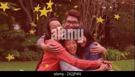 Immagine di stelle d'oro su genitori asiatici sorridenti, figlio e figlia che abbracciano in giardino Foto Stock