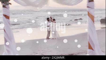 Immagine di macchie bianche sulla sposa afroamericana e lo sposo danzano sulla spiaggia al matrimonio Foto Stock