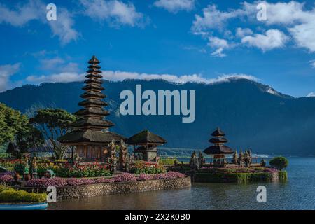 Una vista panoramica di un tradizionale tempio balinese circondato da vividi giardini floreali e adagiato sullo sfondo di una montagna. L'immagine cattura la cultura Foto Stock