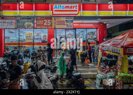 Una scena movimentata all'esterno di un minimarket luminoso di notte, che cattura gli acquirenti, le conversazioni e varie attività intorno a motociclette e S. Foto Stock