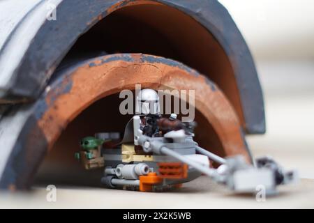 Le minifigure LEGO Mandalorian e Baby Yoda (Grogu) attraversano un tunnel scuro con sfondo sfocato Foto Stock