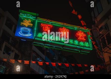 Vivaci cartelli al neon che mostrano i simboli del caffè e del tè in caratteri cinesi a Hong Kong, illuminano una strada urbana di notte adornata di bandiere. Foto Stock