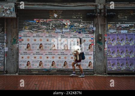 Una dinamica scena urbana che cattura un pedone che cammina frettolosamente davanti a un muro intonacato di volantini pubblicitari colorati. Il contrasto tra il movimento e. Foto Stock