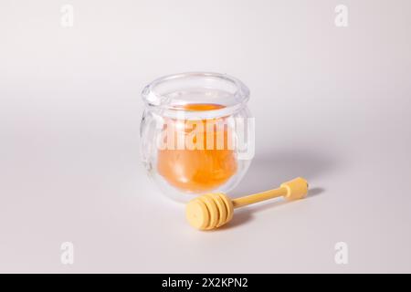 Un bicchiere di miele liquido con un cucchiaio di miele su sfondo bianco Foto Stock