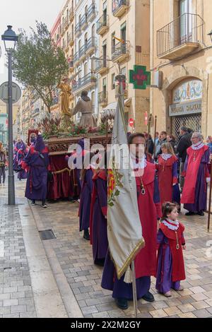 Tarragona, Spagna - 23 aprile 2024: Tradizionale processione con penitenti di viola su una strada acciottolata circondata da vecchi edifici e da un osservatore Foto Stock