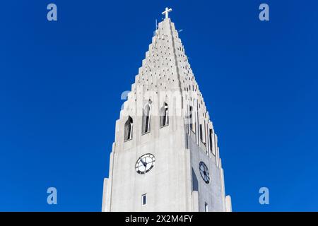 Torre della chiesa di Hallgrimskirkja con Croce Santa e orologio, Reykjavik, Islanda, moderno campanile contro il cielo azzurro. Foto Stock