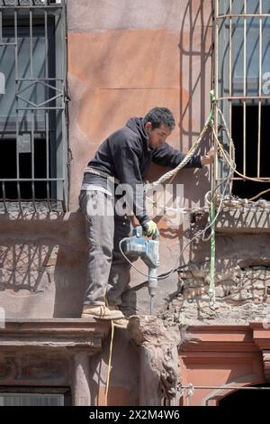 Un operaio edile in una posizione precaria rompe il cemento con il martello. Una ristrutturazione di una vecchia casa in Bedford Ave a Williamsburg, New York. Foto Stock