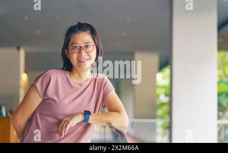 Ritratto di una bella donna asiatica con occhiali da vista in un resort, che indossa casual, sorride e guarda la macchina fotografica, donna asiatica di mezza età a 38-40 anni Foto Stock