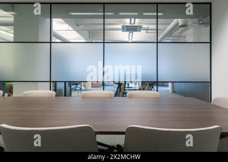 Una sala conferenze elegante e moderna dotata di un grande tavolo in legno, comode sedie, divisori in vetro smerigliato e soffitto industriale Foto Stock