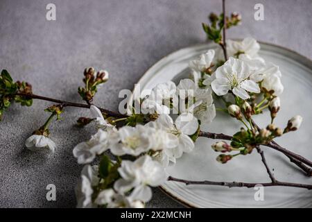 Un sofisticato tavolo con delicati fiori di ciliegio disposti su un elegante piatto di ceramica, che evoca un ambiente sereno in primavera Foto Stock