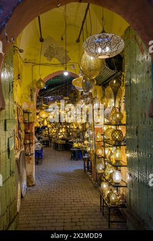 Una vista accattivante di un negozio di lanterne marocchine fiancheggiato da intricate lampade in metallo che proiettano un caldo bagliore nel vivace vicolo del mercato. Foto Stock