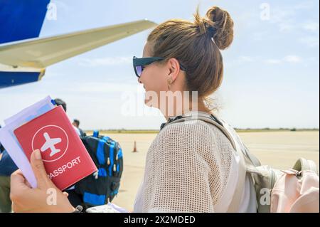 Vista laterale di una donna felice con gli occhiali da sole in possesso del passaporto mentre è in fila per entrare in aereo all'aeroporto in Marocco Foto Stock