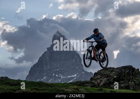 Un mountain bike cavalca su terreni accidentati sullo sfondo maestoso di un picco di montagna sotto un cielo nuvoloso Foto Stock