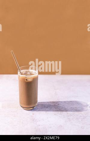 Caffè ghiacciato in un bicchiere alto con una paglia su uno sfondo dai toni caldi, che riflette un'atmosfera estiva rilassata Foto Stock