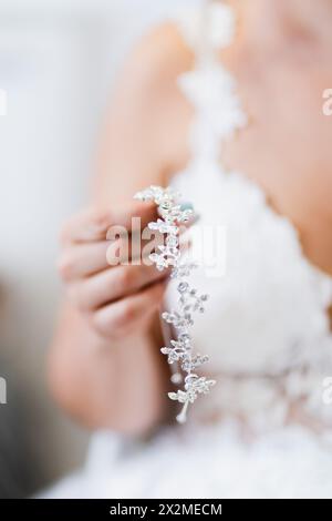 Primo piano di una sposa che regge il suo capo in argento dal design complesso, con un'attenzione morbida sul suo abito da sposa Foto Stock