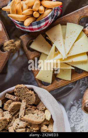 Un piatto rustico con fette di formaggio gourmet e grissini croccanti e biscotti, disposti su un vassoio di legno Foto Stock