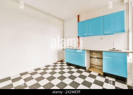Gli interni vuoti della cucina vintage con armadi blu e pavimento a scacchi hanno bisogno di essere rinnovati. Foto Stock