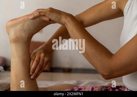 Una donna latina sdraiata sulla schiena riceve un massaggio ayurvedico sul piede, nelle mani in primo piano di una massaggiatrice donna. Conce per massaggio curativo Foto Stock