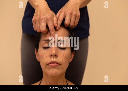 Donna latina che riceve un massaggio ayurvedico sul viso con punti di pressione specifici Foto Stock