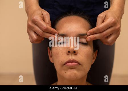 Donna latina che riceve un massaggio ayurvedico sul viso con punti di pressione specifici Foto Stock