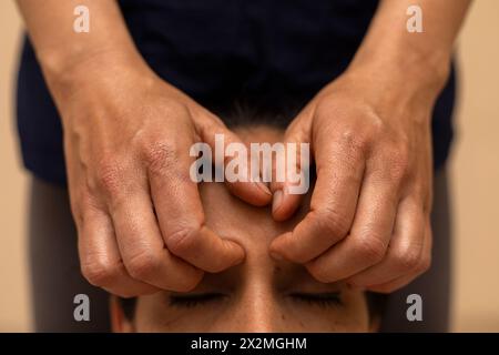 Donna latina che riceve un massaggio ayurvedico sul viso con punti di pressione specifici Foto Stock