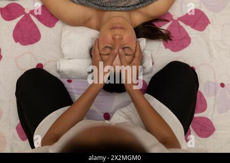 Donna latina che riceve un massaggio Shiroadhyanga sul viso con punti di pressione specifici Foto Stock