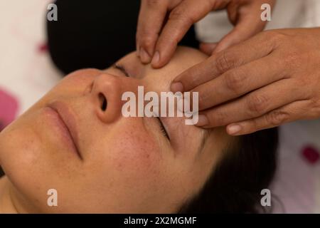 Donna latina che riceve un massaggio Shiroadhyanga sul viso con punti di pressione specifici Foto Stock