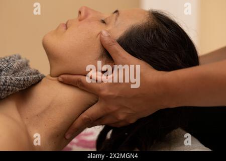 Donna latina che riceve un massaggio Shiroadhyanga sul viso con punti di pressione specifici Foto Stock