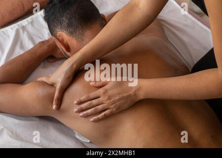 Uomo latinoamericano disteso sulla schiena che riceve un massaggio ayurvedico alle spalle Foto Stock