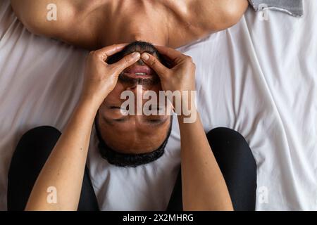 Uomo latino che riceve un massaggio ayurvedico sul viso con punti di pressione specifici Foto Stock
