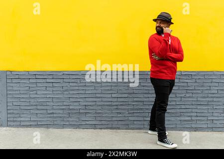 Adulto Latino maschio (39) con barba, in piedi e guardando dietro di lui con un gesto di ricerca di qualcosa. Indossa cappello, maglione rosso e flann bianco Foto Stock