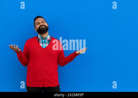 Uomo adulto con barba (39 anni), fa un gesto anticonformista e allunga entrambe le braccia in questione, indossando maglione rosso, camicia a quadri, occhiali scuri, BL Foto Stock