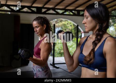 Due donne dell'America Latina eseguono allenamenti funzionali ad alta intensità in palestra utilizzando manubri. Concetto di stile di vita sano Foto Stock