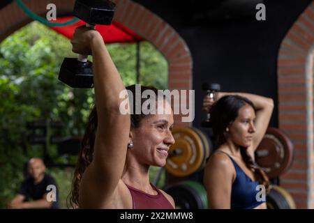 Due donne dell'America Latina eseguono allenamenti funzionali ad alta intensità in palestra utilizzando manubri. Concetto di stile di vita sano Foto Stock