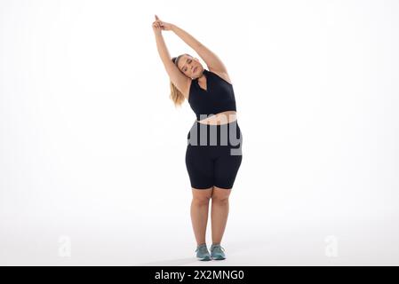 Il modello caucasico Plus-size in sportswear si estende su uno sfondo bianco Foto Stock