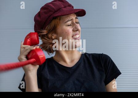 Breve scatto medio di una giovane donna latinoamericana (22) con cappello e capelli rossi scomodi a causa delle urla che sente dalla conversazione su t Foto Stock
