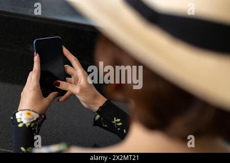 Giovane ragazza latinoamericana (22) con cappello da cowboy usando il suo cellulare. Concetto di tecnologia e vacanza Foto Stock