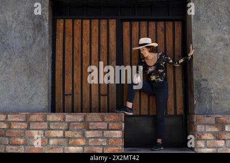 Giovane ragazza latino-americana (22) con cappello da cowboy posa davanti all'ingresso in legno sullo sfondo. Copia spazio. Concetto del modello Foto Stock