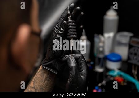 Tatuatore che assembla l'ago sterilizzato nell'impugnatura. Indossare guanti neri. Concetto di Body art Foto Stock