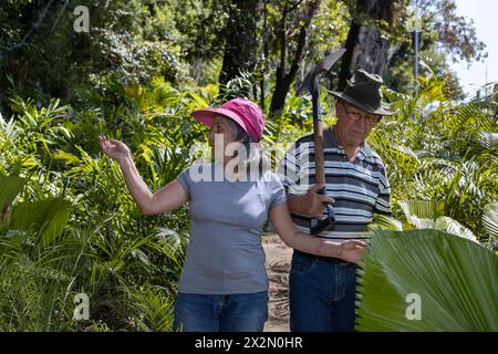 Due anziani dell'America Latina camminano attraverso il loro giardino sul retro, pensionati e concetto di tempo libero Foto Stock