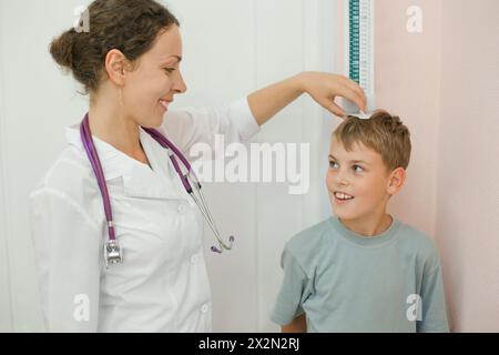 Medico misura crescita sorridente ragazzo in studio medico, concentrarsi su medico Foto Stock