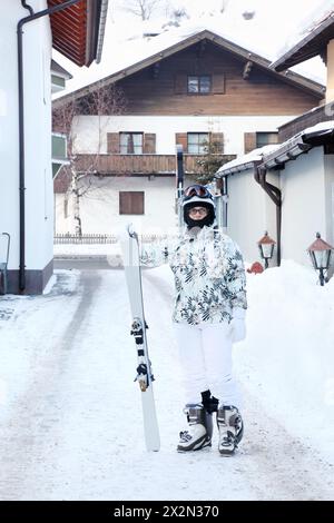 Donna che indossa una tuta sportiva bianca e un casco con lo snowboard nel villaggio di montagna. Foto Stock