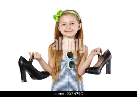 Ragazza sorridente con supporti per prendisole a righe, tenendo in mano grandi scarpe da madre nere Foto Stock