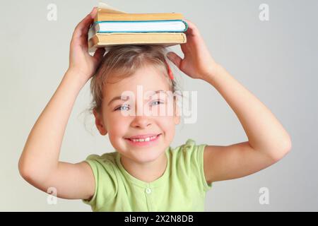 Una bambina sorridente tiene i libri in testa Foto Stock