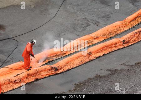 Il lavoratore lava la barra di taglio arancione con l'acqua dal tubo flessibile. Le barre antiscivolo consentono di individuare le aree in cui potrebbero verificarsi fuoriuscite di petrolio nelle acque portuali Foto Stock
