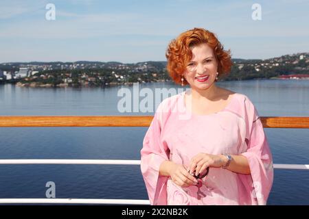 Happy Woman si trova vicino alla ringhiera sul ponte della nave sullo sfondo di una splendida costa Foto Stock